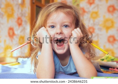 cute girl with blond red hair with emotions of joy and pranks on her face with pencils in her hands. Face close-up. home education. Sincere childhood emotions are genuine. Home furnishings. Royalty-Free Stock Photo #2438646231