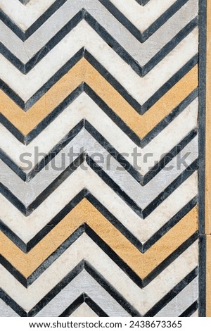 Chevron pattern wall texture background. Marble inlay art work in Yellow grey black white Chevron pattern. Design of precious stones on marble walls of Taj Mahal. Vintage design of chevron pattern.