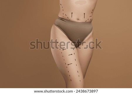 liposuction, fat and cellulite removal. Lifting and anti-age concept. Young woman with massage lines and arrows on her body touching skin on leg, beige studio background