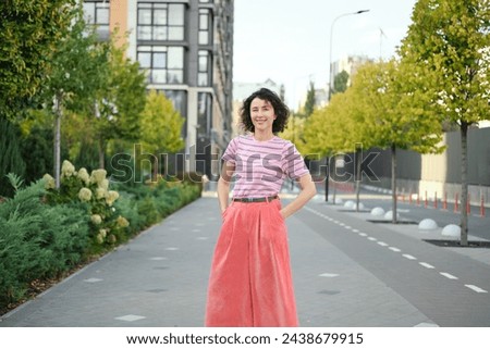 Happy young woman walking outside. One confident girl walks outdoors in street smiling. Urban city, residential complex, real estate concept. Brunette female adult in pink clothes. High quality photo