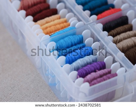 A close-up shot of a plastic sorting box full of bobbins with different colour embroidery threads on a beige canvas background. Royalty-Free Stock Photo #2438702581