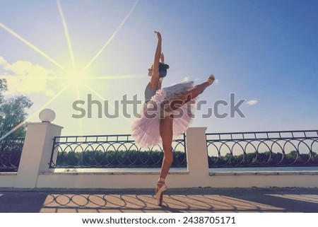 a ballerina in a tutu bodysuit and pointe shoes with beautiful feet makes an arabesque on a summer day on the terrace Royalty-Free Stock Photo #2438705171