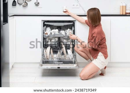 Busy housewife putting dirty plates in dishwasher machine in the kitchen. Household and exhausting cleaning day concept Royalty-Free Stock Photo #2438719349