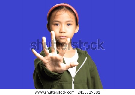 Oops! Surprised little Asian girl doing stop sign with palm on blue background. Focus on palm with blur background.