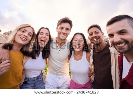 Bunch of happy multiracial friends having fun outdoors at the park. Diverse group of cheerful joyful young people standing up looking at the camera and smiling all together. They are hug and laugh