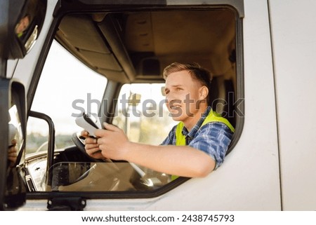 Truck driver job. Logistics - proud driver or forwarder on truck and trailer, on a transshipment point. Transportation service. Royalty-Free Stock Photo #2438745793