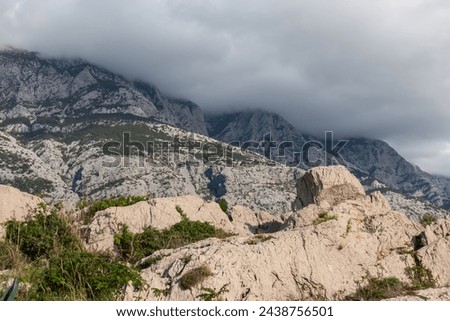Panoramic view of cloud covered Biokovo mountain range in majestic Dinaric Alps seen from Makarska, Split-Dalmatia, Croatia, Europe. Coastline of Makarska Riviera. Hiking in the Balkans. Wanderlust Royalty-Free Stock Photo #2438756501