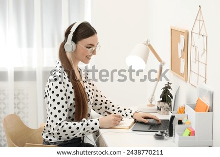 E-learning. woman taking notes during online lesson at table indoors