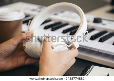 White headphones in the hands of a female musician at the workplace with a piano keyboard. A synthesizer for home practice, remote music lessons, music creation.