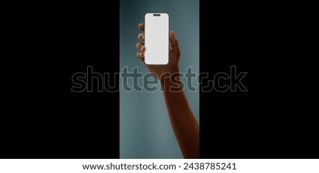 Black African-American hand displays a modern smartphone with a blank screen against a deep teal background, ideal for presenting apps or mobile interfaces in a clean and contemporary setting Royalty-Free Stock Photo #2438785241