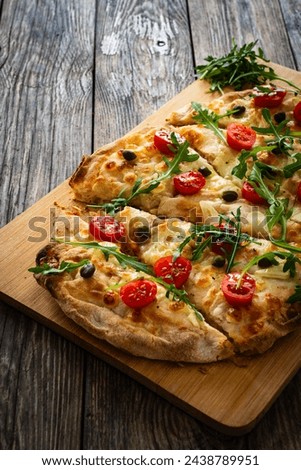 Roman pinsa with mozzarella cheese, capers, arugula and garlic on wooden table 