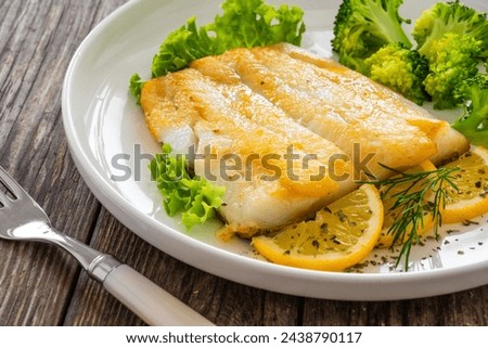 Seared halibut fillet, sliced lemon and boiled broccoli on wooden table 