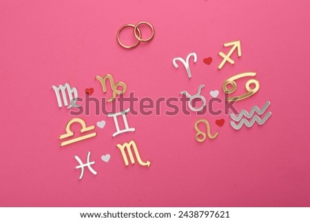 Zodiac compatibility. Signs and wedding rings on pink background, flat lay Royalty-Free Stock Photo #2438797621