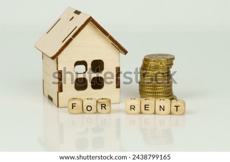 Wooden model of a house next to coins and wooden cubes with the inscription - for rent.
