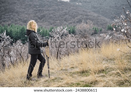 Beautiful smiling adult woman against the background of blossoming almond trees in the mountains, Nordic walking and active lifestyle, free space for concept