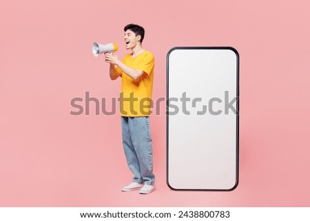 Full body young man wear yellow t-shirt casual clothes big huge blank screen mobile cell phone smartphone with copy space mockup area scream in megaphone isolated on plain pastel light pink background