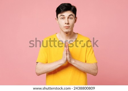 Young Caucasian man wears yellow t-shirt casual clothes hold hands folded in prayer gesture, begging about something isolated on plain pastel light pink color wall background studio. Lifestyle concept Royalty-Free Stock Photo #2438800809