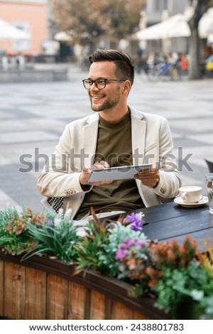 Thoughtful businessman holding a digital tablet and looking away. Contemplative young businessman sitting in an outdoor Cafe.