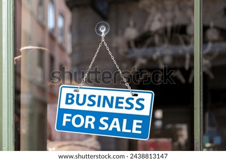 Close-up on a white and blue sign in a window written inside it "Business for sale".

