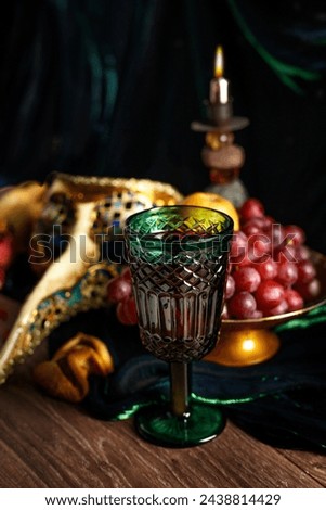 Multicolor carnival mask, wine, burning candle on a dark wooden table. Purim, Mardi Gras holiday concept. Rustic.