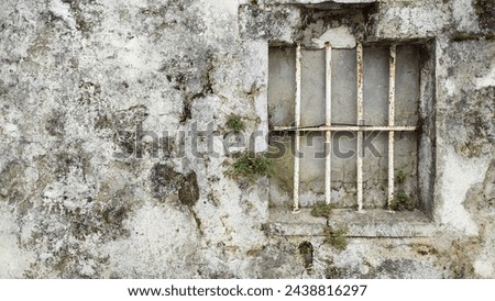 Ventana antigua con reja de hierro en la antigua pared agrietada. Bar on an old window placed on a cracked wall. Royalty-Free Stock Photo #2438816297