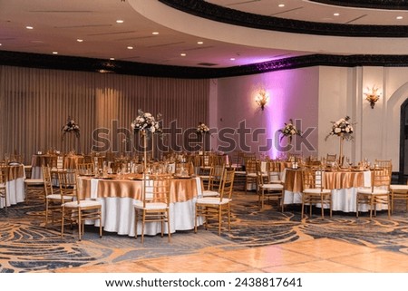 A banquet hall with tables and chairs set up for a wedding reception. Royalty-Free Stock Photo #2438817641