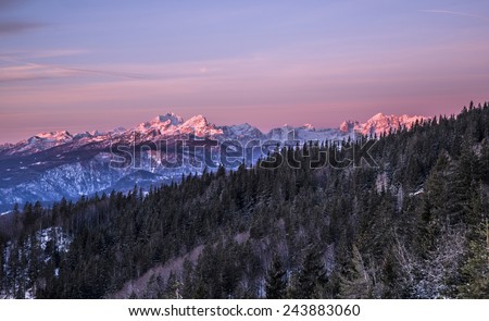 Purple Sunrise in the Hills & Forest. Snowy mountains on an early winter morning. Photograph was taken in Slovenia on the border with Austria. Panorama with forest, mountains, clouds and clear sky.
