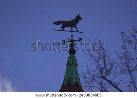 A fox weather vane, wind vane, or weathercock, showing the direction of the wind. This architectural ornament sits on the filial of a Victorian home. Royalty-Free Stock Photo #2438834883