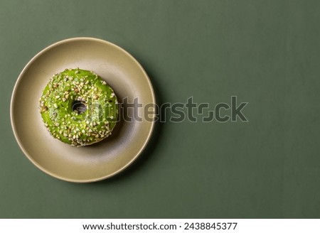 Appetizing, pistachio donut on a plate and on a colored background. Flat lay, with space for text.