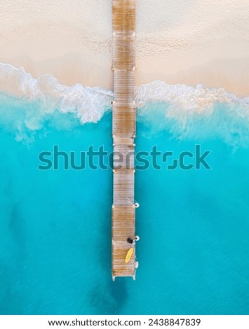 vertical aerial of yellow kayak and black bag on wooden pier surrounded by prettiest blue water and waves crashing on the white sandy shore of Grace Bay Beach