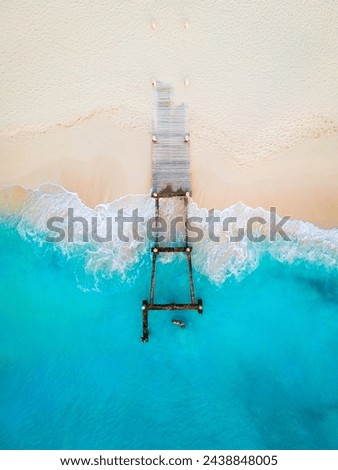 top down angle of old rusty pier destroyed by hurricane on clean empty white sand beach with blue waves crashing in 