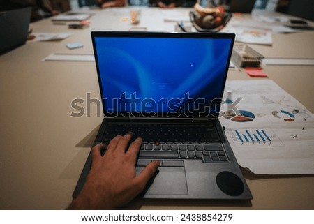 Close-up of a professional's hands typing on a laptop with colorful business analytics and charts spread out on the office desk.