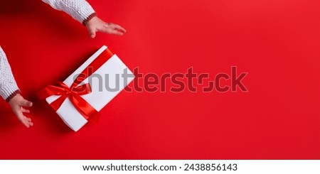 Baby hands holding gift box on red background. template, banner, christmas concept, copy space.