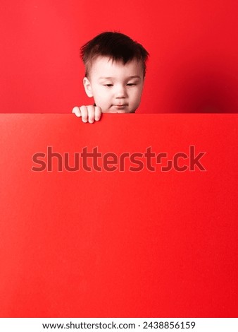 Baby in red flannel shirt on red background. Child's emotions, template, blank, looking at text, copy space.