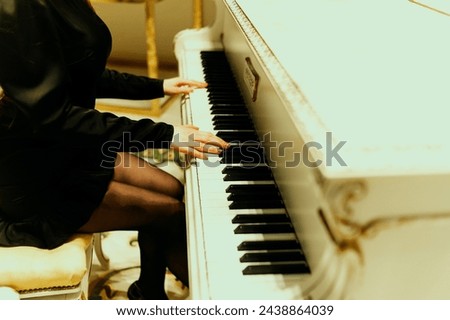 Young woman in black dress plays a white piano. Classical music concert. Professional playing on keyboard musical instruments. Female hands on the keys of a white piano.