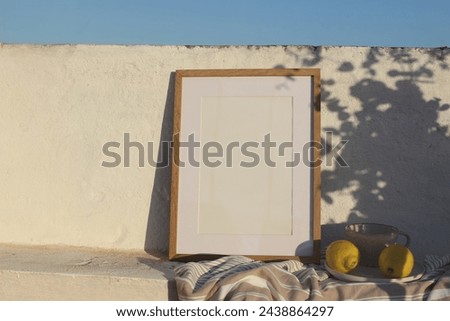 Vertical wooden frame picture mockup against white old textured white wall in sunlight. Fresh yellow lemons fruit, cup of coffee. Mediterranean summer background with light, floral shadows, blue sky.