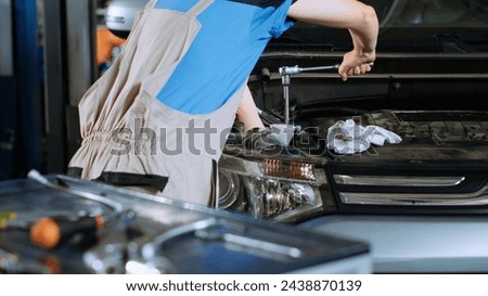 Close up shot of mechanic in garage using torque wrench to tighten bolts inside opened up vehicle after changing oil. Car service employee doing maintenance on automobile, removing leftover spillage Royalty-Free Stock Photo #2438870139