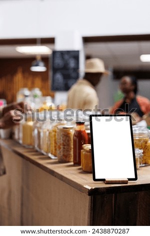 Close-up of phone tablet displaying an isolated copyspace template is seen at an eco friendly food shop. Focused image of a digital device with an empty mockup display, placed near bio-food products.