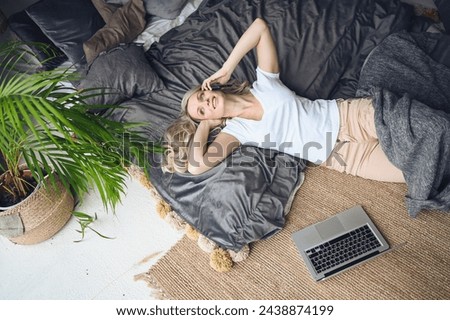 Blonde woman speaking phone working, making video call, watching movie on a laptop in cozy home bedroom modern interior. Home quarantine Covid-19 pandemic Corona virus. Remote work from home concept. Royalty-Free Stock Photo #2438874199