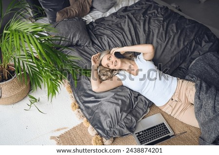 Blonde woman speaking phone working, making video call, watching movie on a laptop in cozy home bedroom modern interior. Home quarantine Covid-19 pandemic Corona virus. Remote work from home concept. Royalty-Free Stock Photo #2438874201