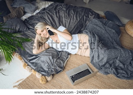 Blonde woman speaking phone working, making video call, watching movie on a laptop in cozy home bedroom modern interior. Home quarantine Covid-19 pandemic Corona virus. Remote work from home concept. Royalty-Free Stock Photo #2438874207