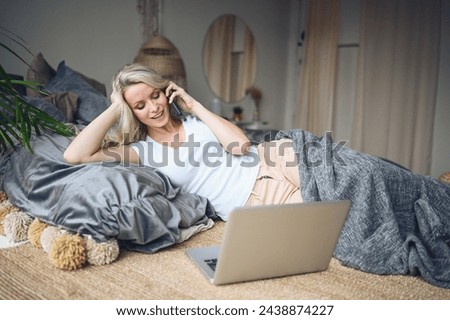 Blonde woman speaking phone working, making video call, watching movie on a laptop in cozy home bedroom modern interior. Home quarantine Covid-19 pandemic Corona virus. Remote work from home concept. Royalty-Free Stock Photo #2438874227