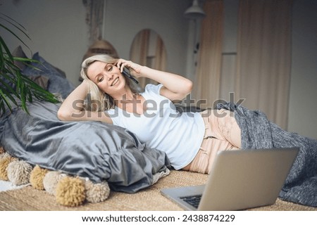 Blonde woman speaking phone working, making video call, watching movie on a laptop in cozy home bedroom modern interior. Home quarantine Covid-19 pandemic Corona virus. Remote work from home concept. Royalty-Free Stock Photo #2438874229