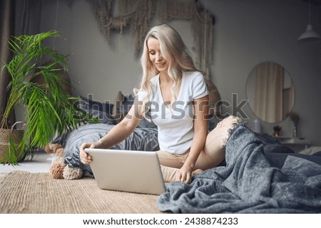 Happy beautiful blonde woman working, making video call, watching movie on a laptop in cozy home bedroom modern interior. Home quarantine Covid-19 pandemic Corona virus. Remote work from home concept. Royalty-Free Stock Photo #2438874233