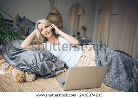 Blonde woman speaking phone working, making video call, watching movie on a laptop in cozy home bedroom modern interior. Home quarantine Covid-19 pandemic Corona virus. Remote work from home concept. Royalty-Free Stock Photo #2438874235