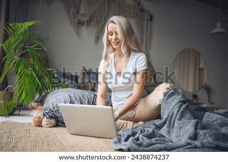 Happy beautiful blonde woman working, making video call, watching movie on a laptop in cozy home bedroom modern interior. Home quarantine Covid-19 pandemic Corona virus. Remote work from home concept. Royalty-Free Stock Photo #2438874237