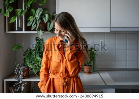 Smiling happy woman enjoy pleasant conversation on cellphone at home. Relaxed Scandinavian middle aged female in orange dress make smartphone call listening funny story. Mobile phone communication. Royalty-Free Stock Photo #2438894915