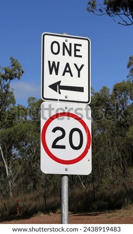 One Way and Speed Limit road signs attached to a grey metal pole with the sky and trees in the background