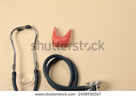 Endocrinology. Stethoscope and model of thyroid gland on beige background, top view. Space for text