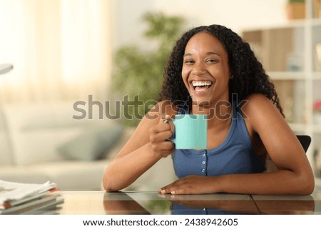 Happy black woman drinking and laughing looking at you at home Royalty-Free Stock Photo #2438942605